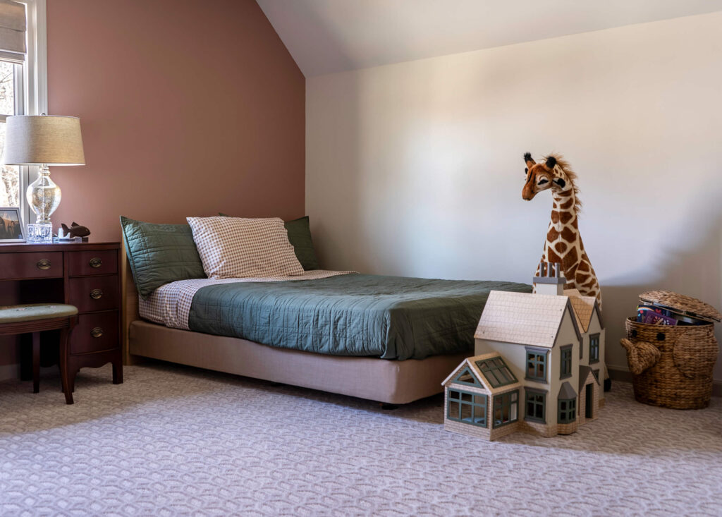 A children's bedroom with patterned carpet, mauve statement wall and dollhouse as decor.