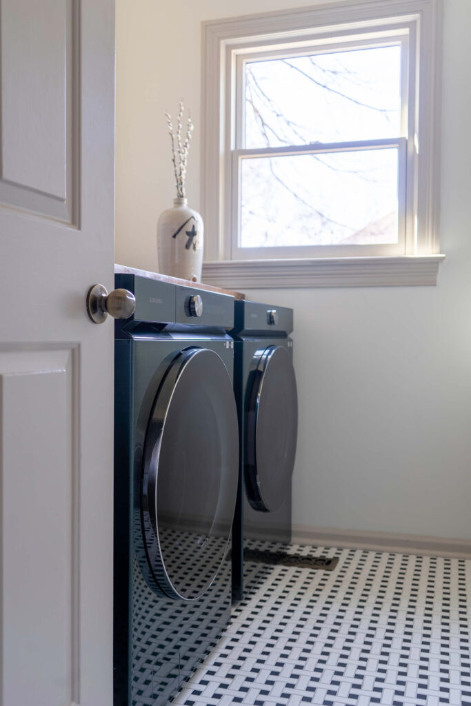 Laundry room design with black washer and dryer, patterned black and white laundry floor tiles, and luxury home design.