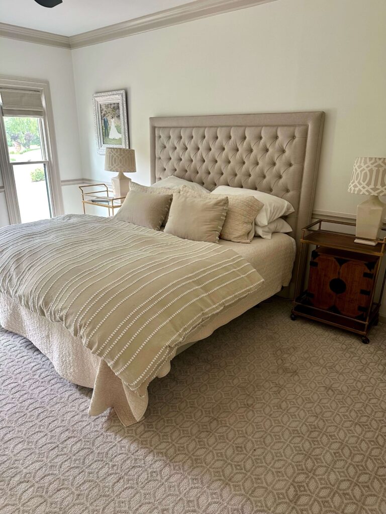 Bedroom with patterned carpet, a tufted headboard and neutral color palette.