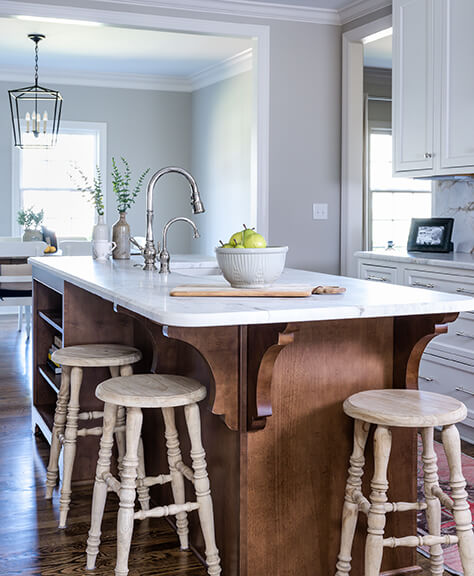 A luxury kitchen with an ornate wood island, rustic barstools and granite countertops.