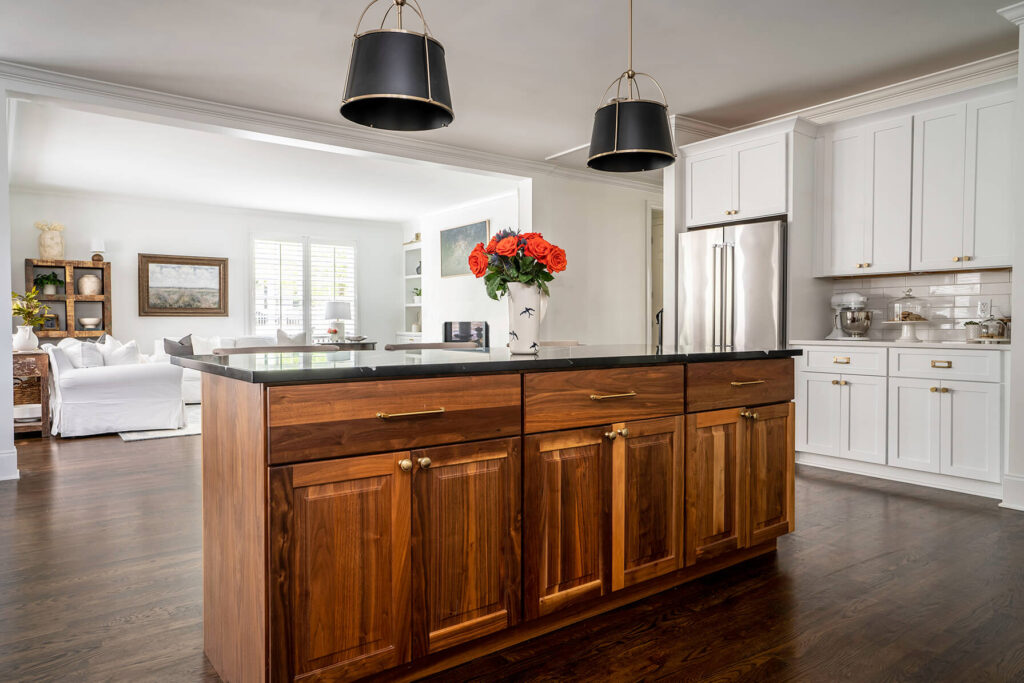 A kitchen island with a wood finish amidst a background of white cabinets and black pendant lighting.