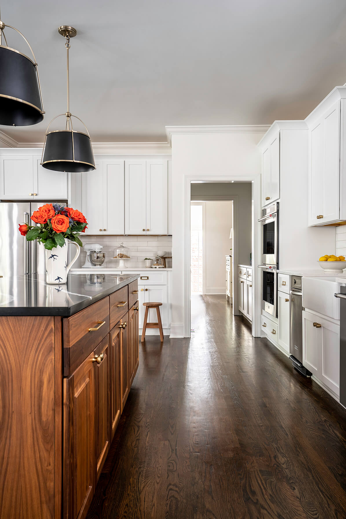 The aisle down a kitchen with dark wood floors, a medium wood island with black countertops.