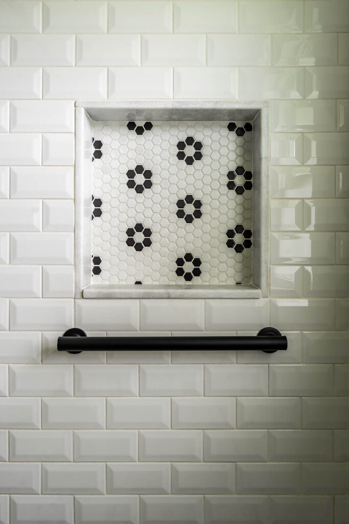 A close up of a shower with a recessed shelf for shampoo and conditioner, with a patterned tile.