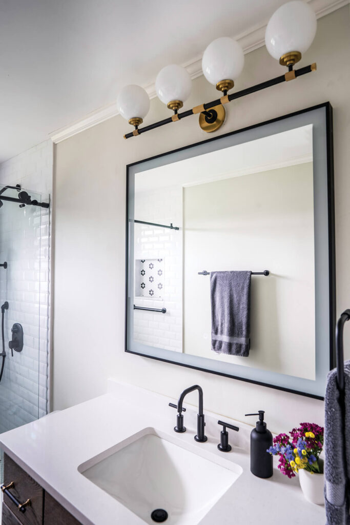 An updated bathroom with large mirror, modern lighting and white countertops.