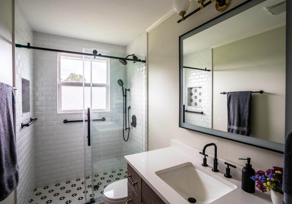 A light and bright bathroom with a large mirror, white countertops and a walk in shower.