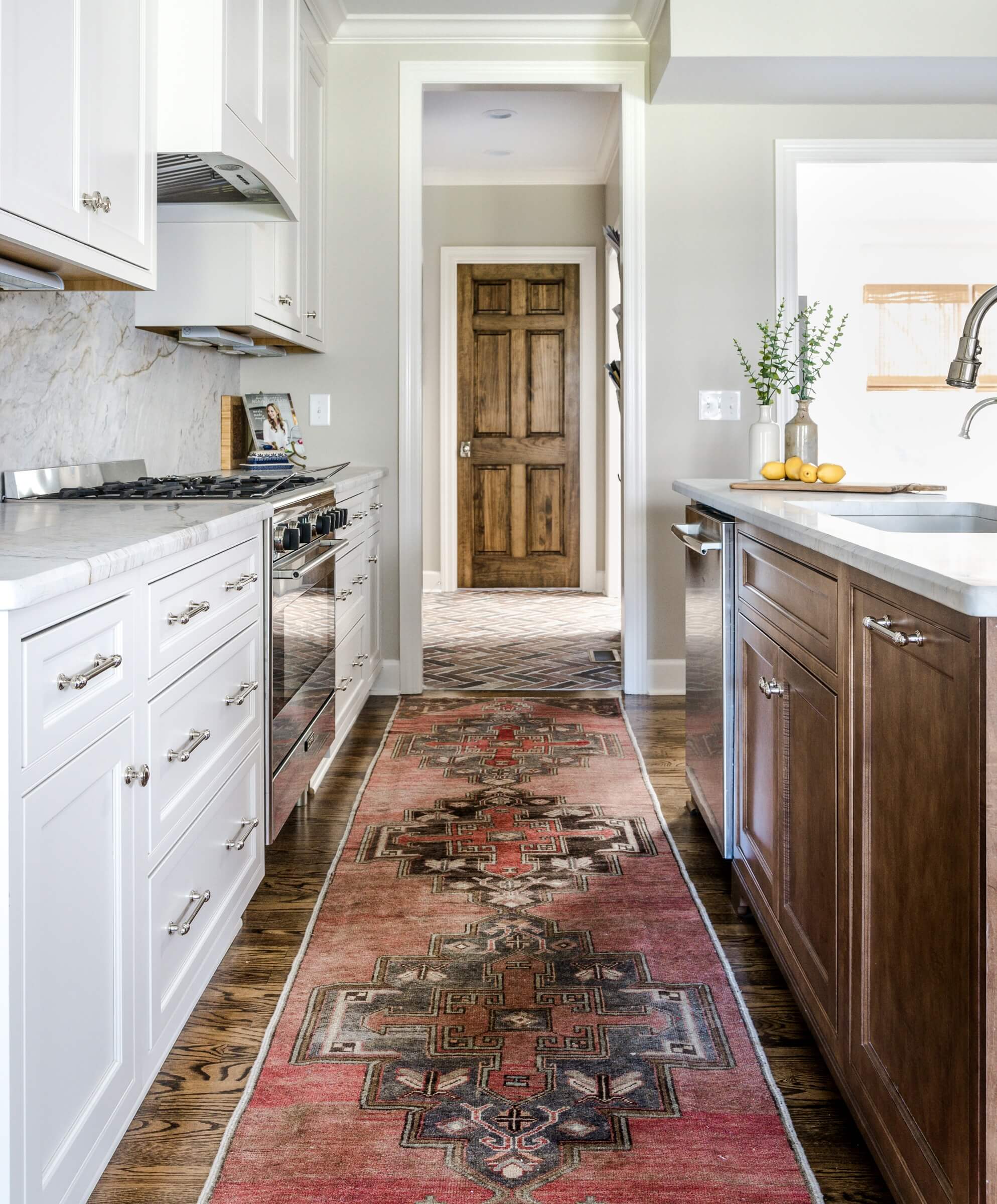 A view of this timeless kitchen down the aisle between the island and stove toward the mudroom.