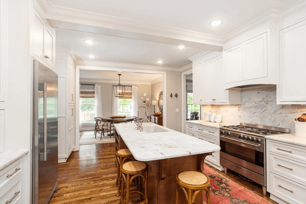 A timeless white kitchen with marble countertops, a marble backsplash, and custom cabinetry.