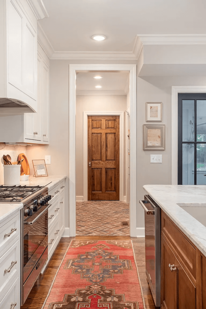 A view down the isle from the kitchen into the mudroom with a brick herringbone flooring and stained wood door